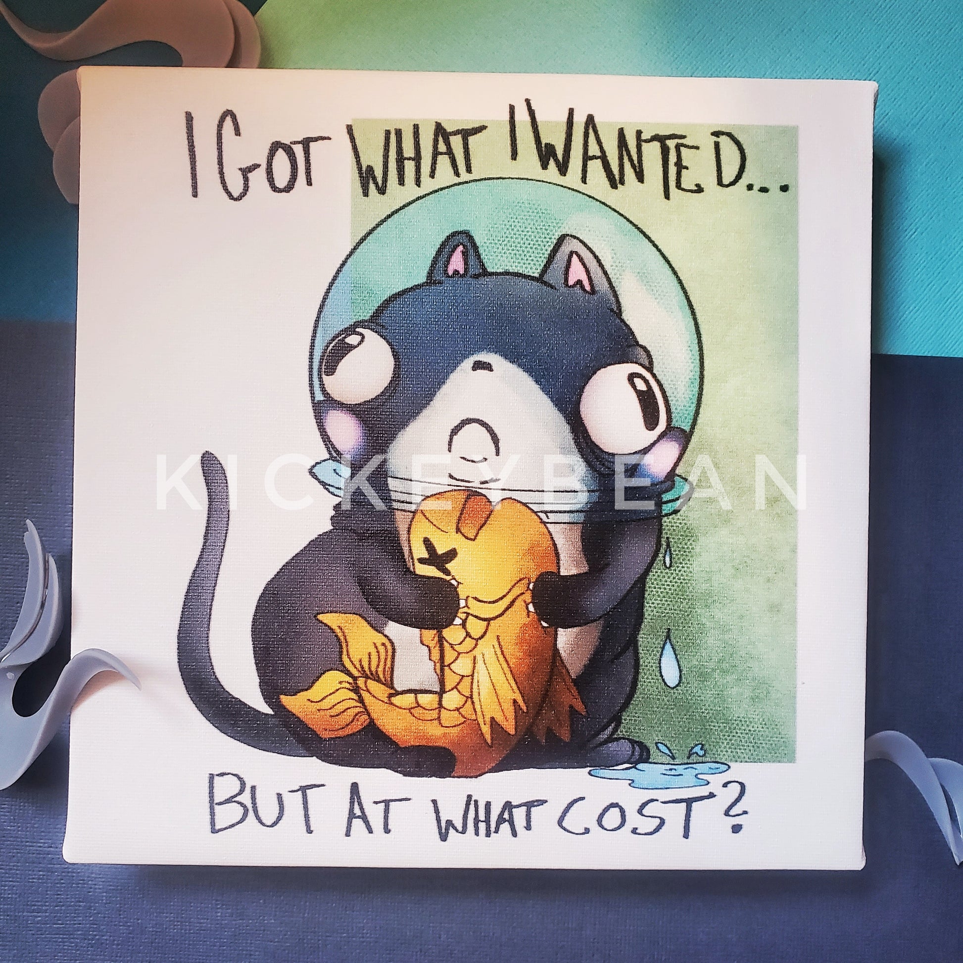 An 8x8 canvas print of a small gray cat holding a fish with the fishbowl stuck on his head. Text reads "I got what I wanted, but at what cost?"